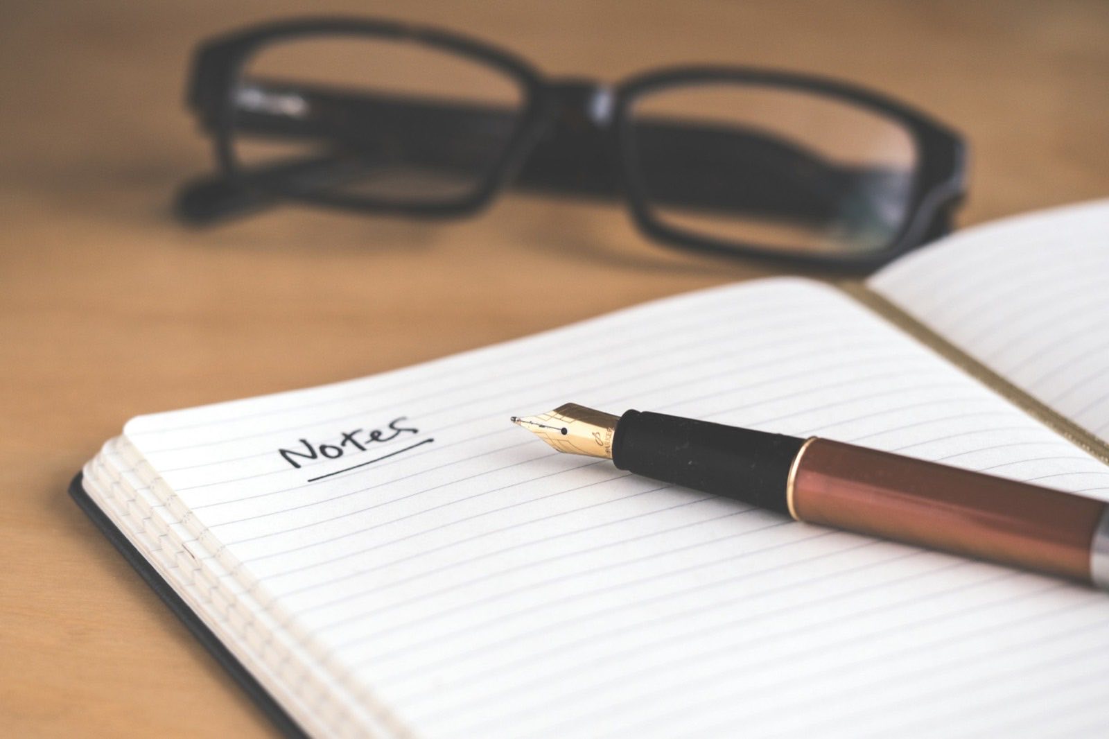 An open notebook, fountain pen, and reading glasses on a desk